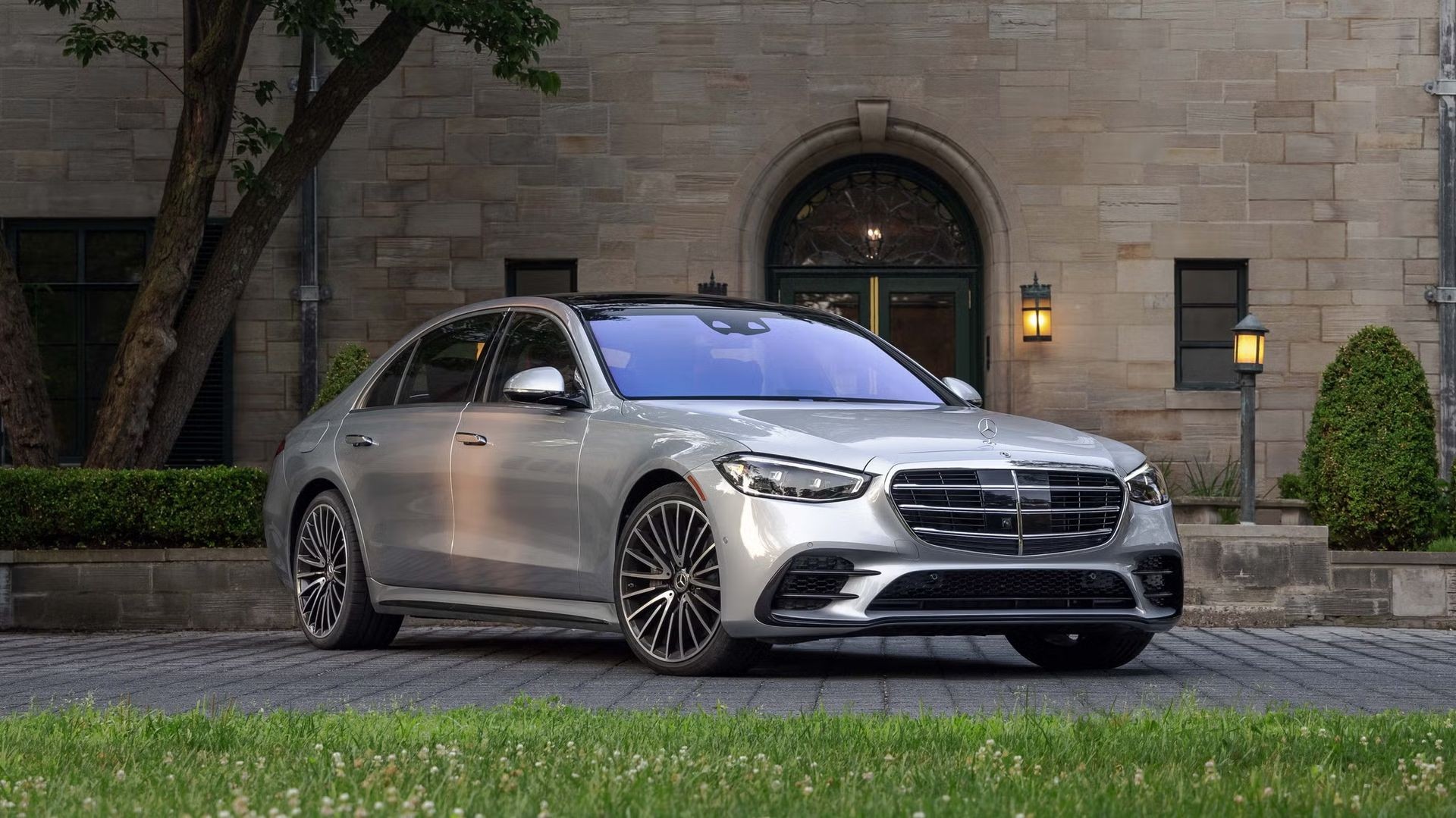 Silver luxury sedan parked in front of a stone building with lantern lights and greenery.